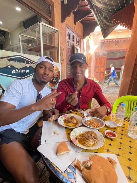 Adil et un visiteur partageant une tanjia à une table de rue